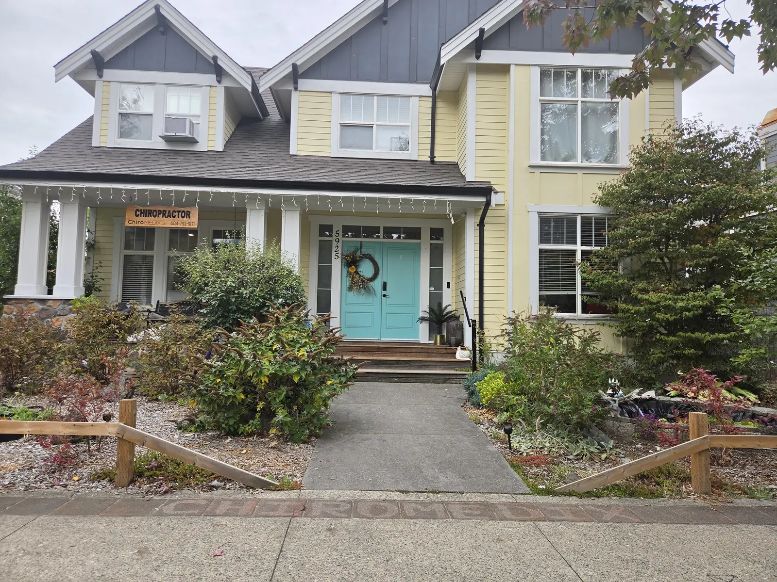 The front of the clinic: a yellow house with a Chiropractor sign on the porch, a teal front door, and ChiroMEDIX set into the sidewalk