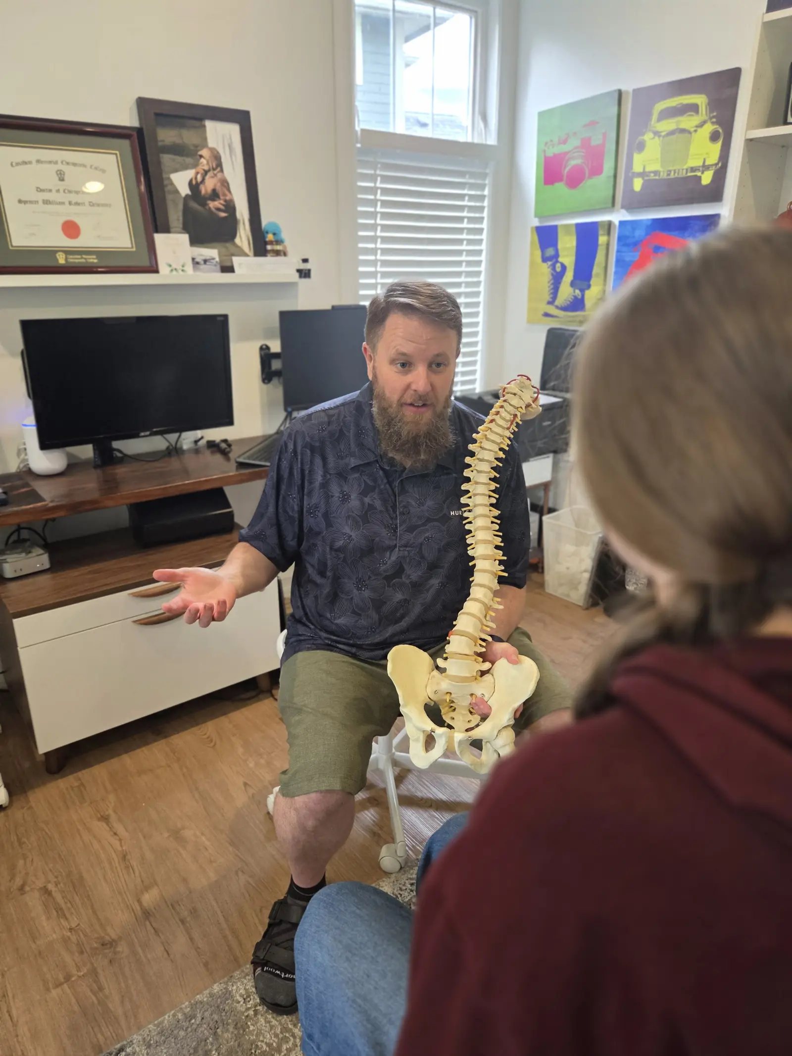 Dr. Devenney explaining a spine model to a patient, pointing to the vertebrae